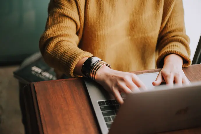 Personne en pull jaune tapant sur un ordinateur portable sur une table en bois